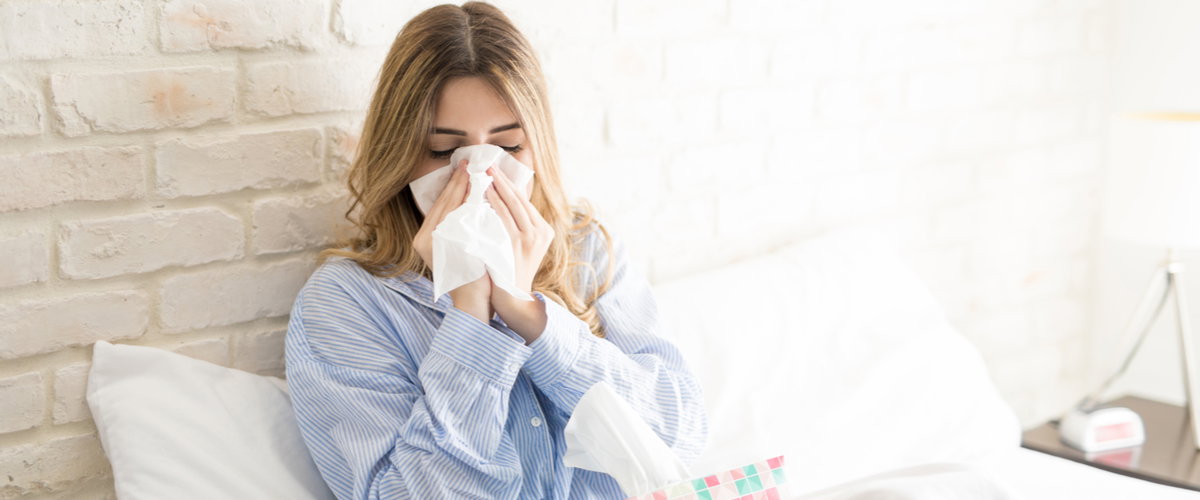 Frau liegt im Bett und putzt sich die Nase