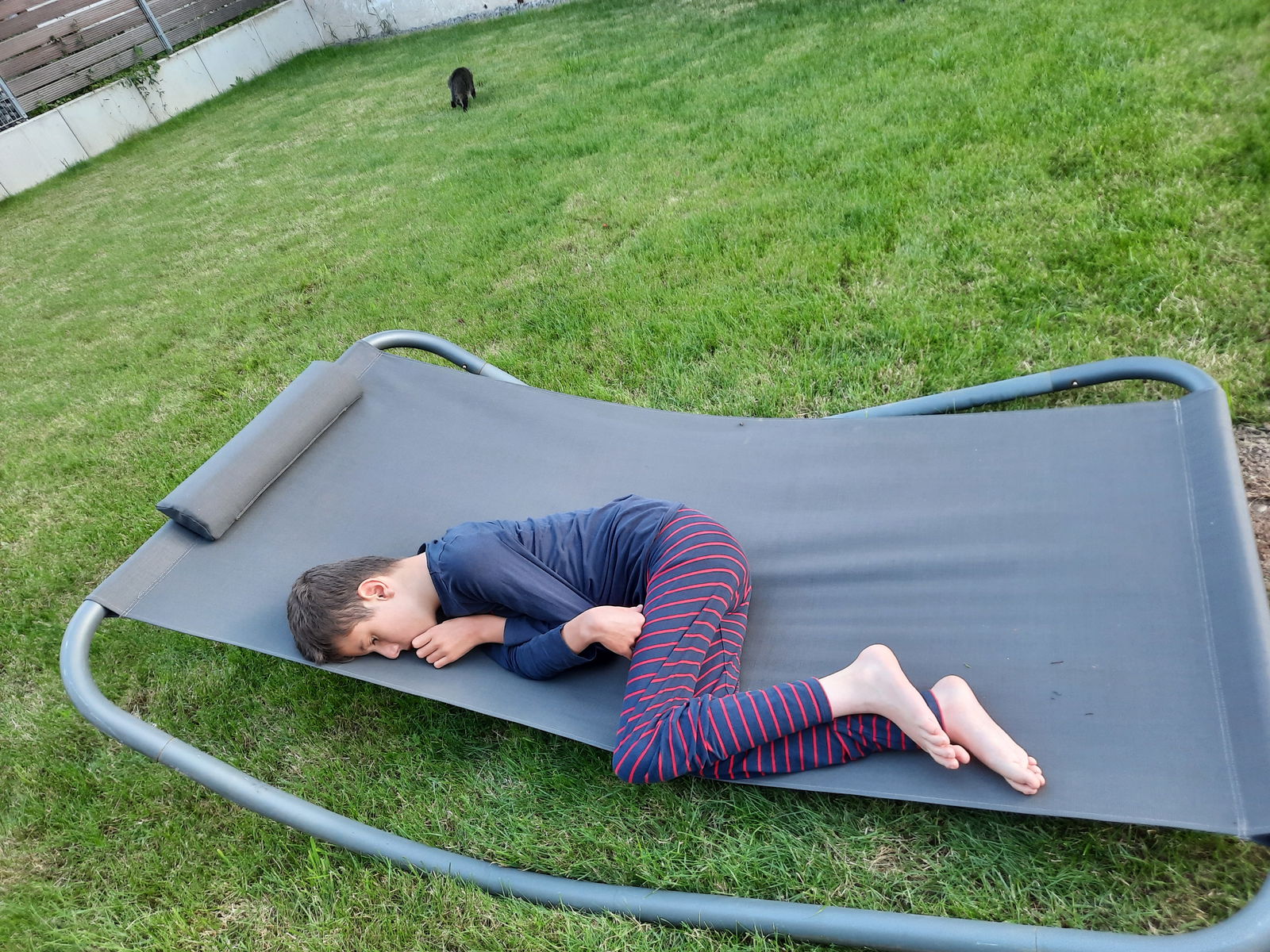 Junge liegt seitlich zusammengekrümmt auf einer Liege auf einer Wiese