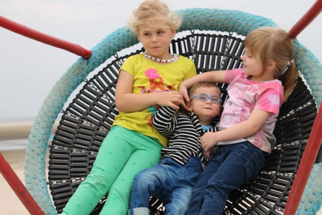 Zwei Schwestern sitzen mit kleinem Bruder in der Mitte auf der Schaukel