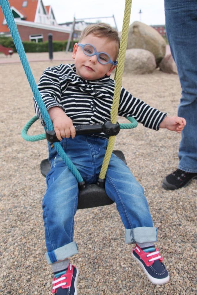 Kleiner Jung mit blauer Brille auf der Schaukel
