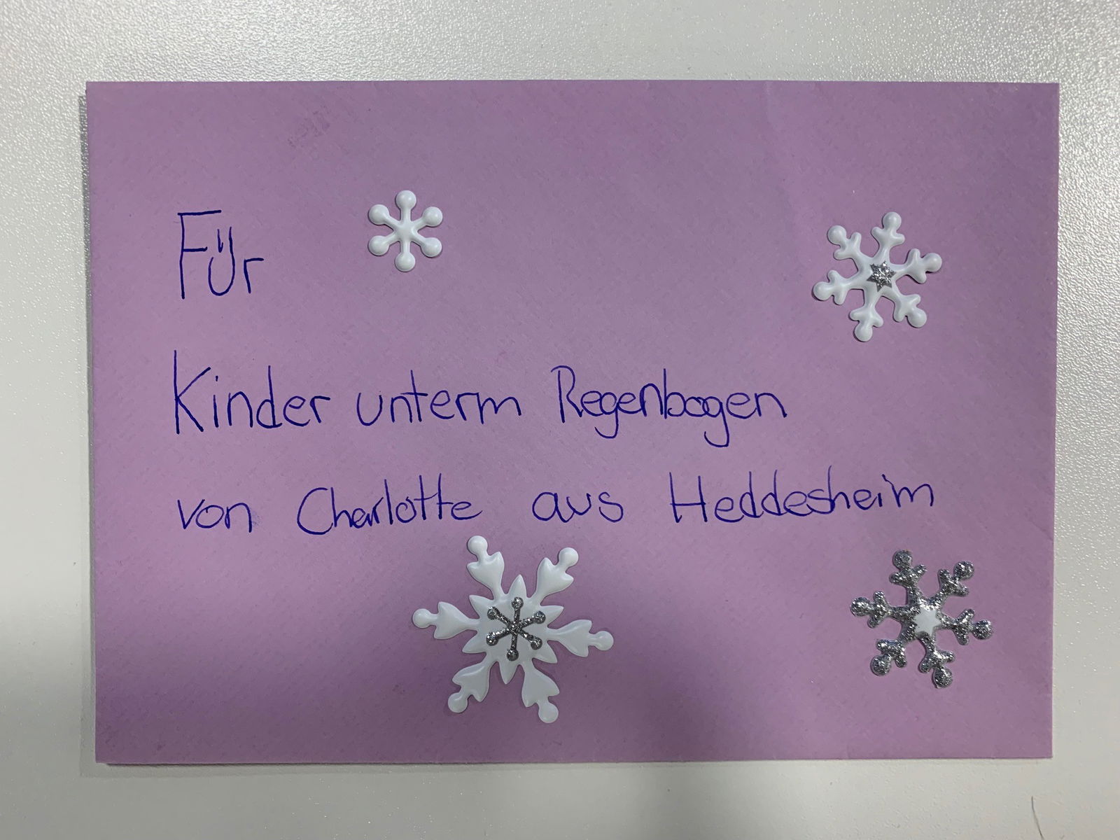Brief in violett mit weißen und silbernen Schneeflocken mit der Anschrift "Für Kinder unterm Regenbogen von Charlotte aus Heddesheim"