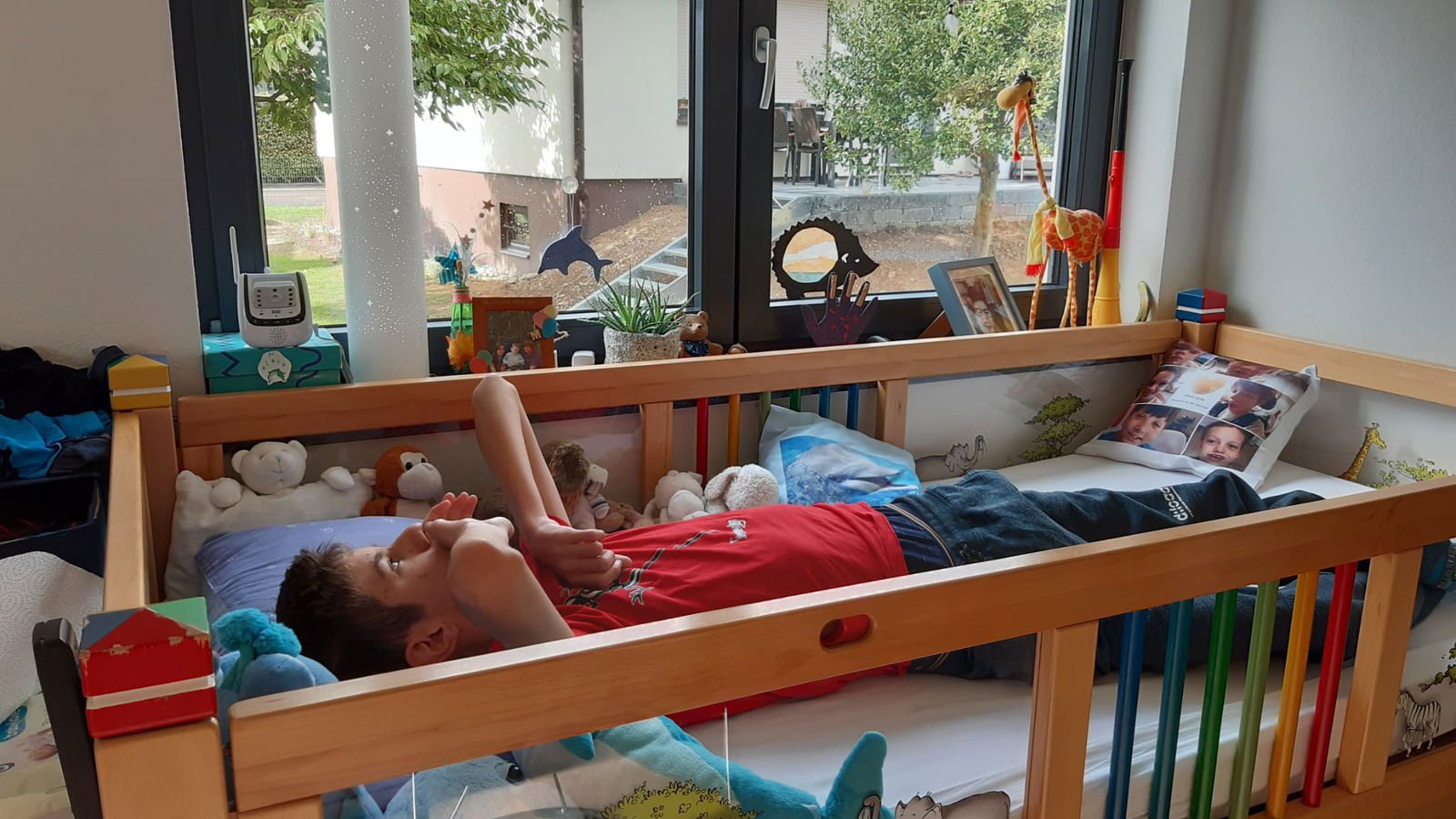 Jugendlicher liegt in einem Bett mit Stofftieren und Gittern