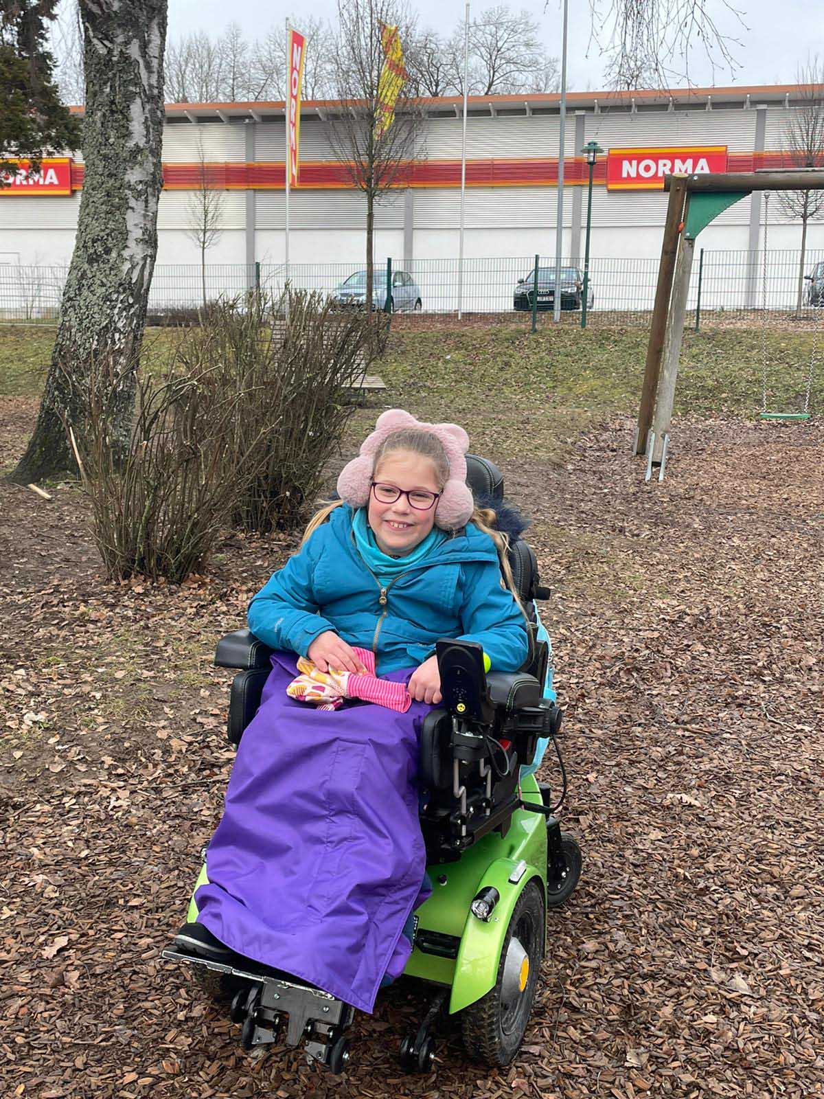 Mädchen mit rosafarbenen, puscheligen, Ohrschützern im Rollstuhl