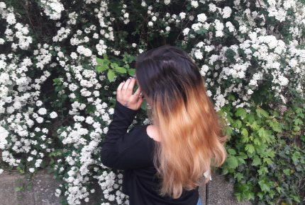 Mädchen mit langen Haaren vor weißen Blumen hält sich die Stirn