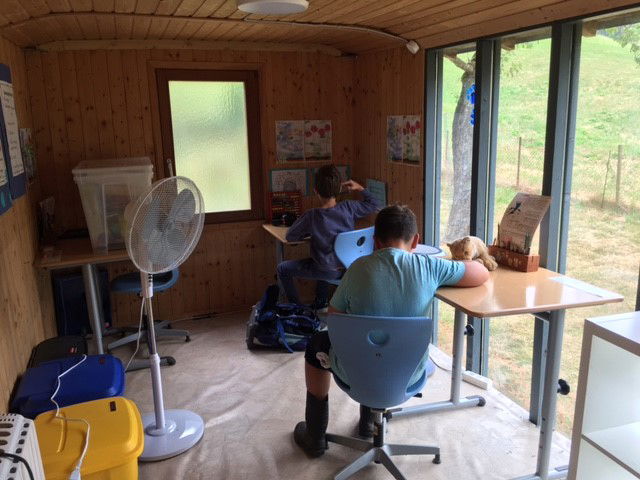 Zwei Kinder an Schreibtischen mit Ventilator in einem Schulbauwagen