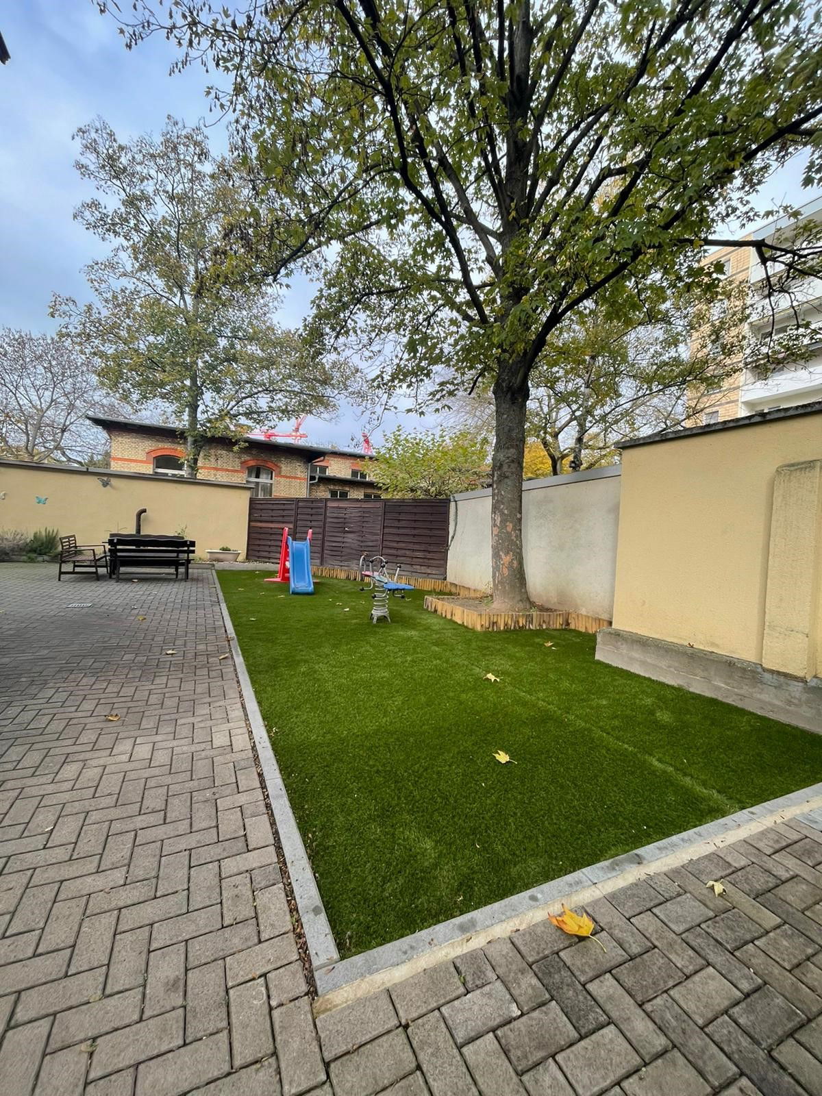 Kinderrutsche auf einem mit Steinen begrenzten grünen Rasen mit Baum