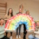 Fünf Frauen halten einen großen gemalten Regenbogen in den Händen