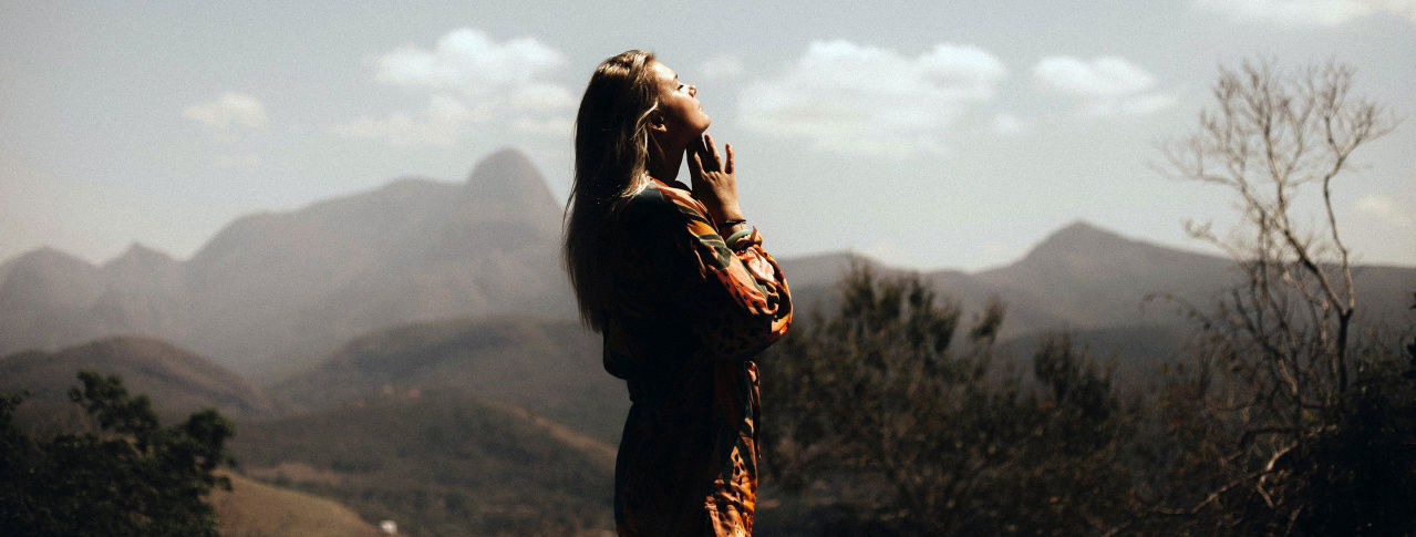Eine Frau steht auf einem Berg und lässt sich die Sonne ins Gesicht scheinen