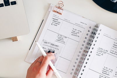 Eine Frau hält einen Stift und notiert sich Termine in einen Kalender 