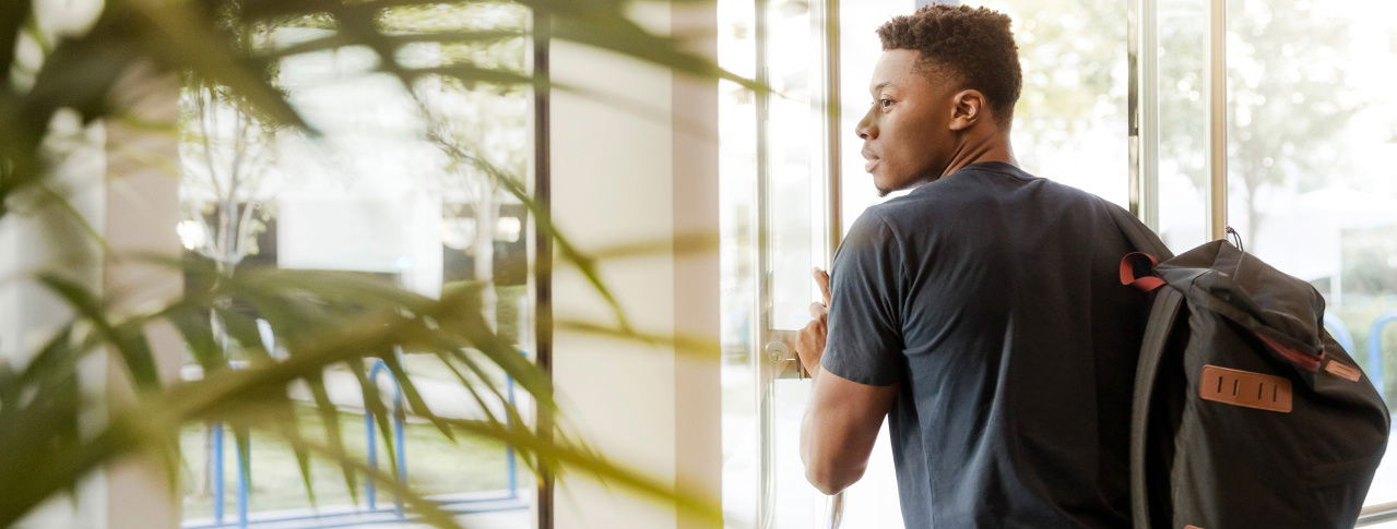 Mann mit Rucksack geht aus Gebäude