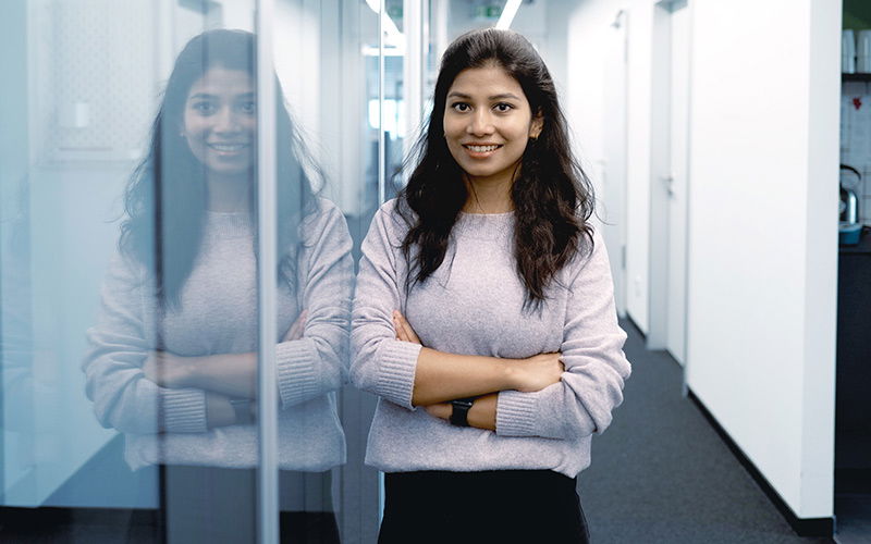 Eine junge Frau lehnt an einer Wand und lacht in die Kamera 