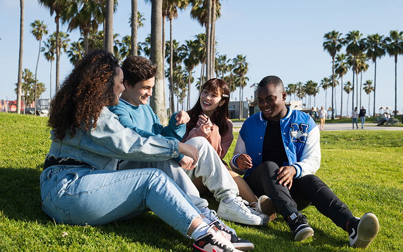 Junge Menschen sitzen auf einer Wiese in Los Angeles und reden miteinander 