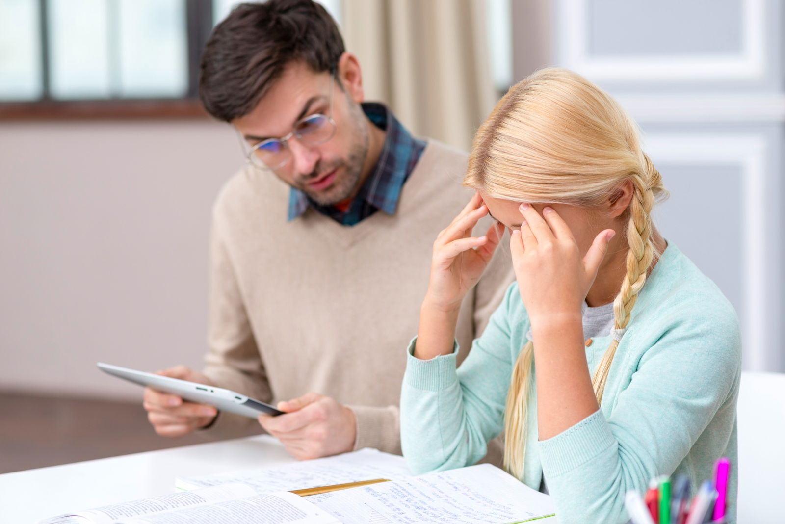 Ein Nachhilfe-Lehrer sitzt neben einer Schülerin, die die Hände am Kopf verschränkt hat und nachdenkt 