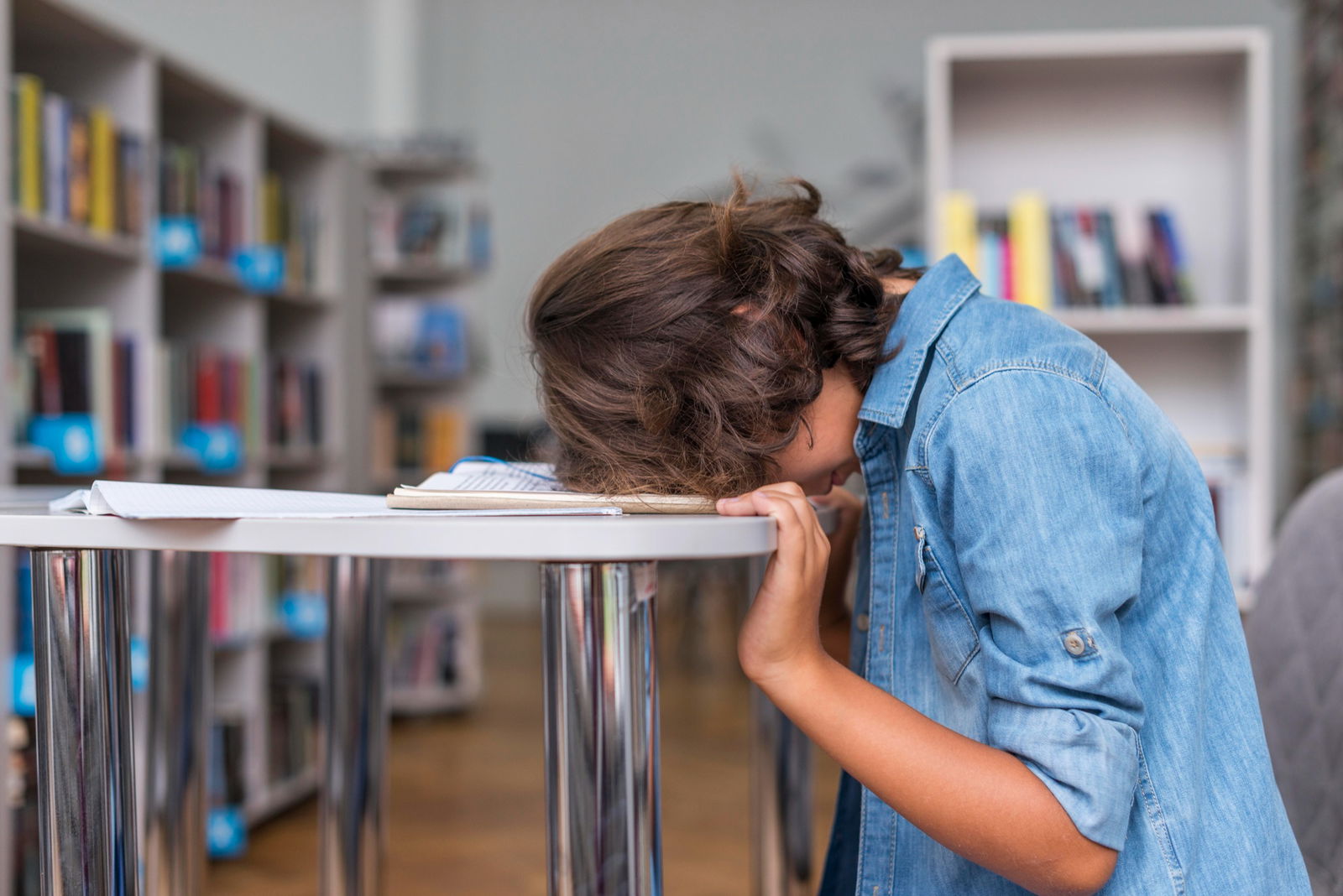 Ein junger Schüler sitzt im Klassenzimmer und legt seinen Kopf erschöpft auf dem Tisch ab 