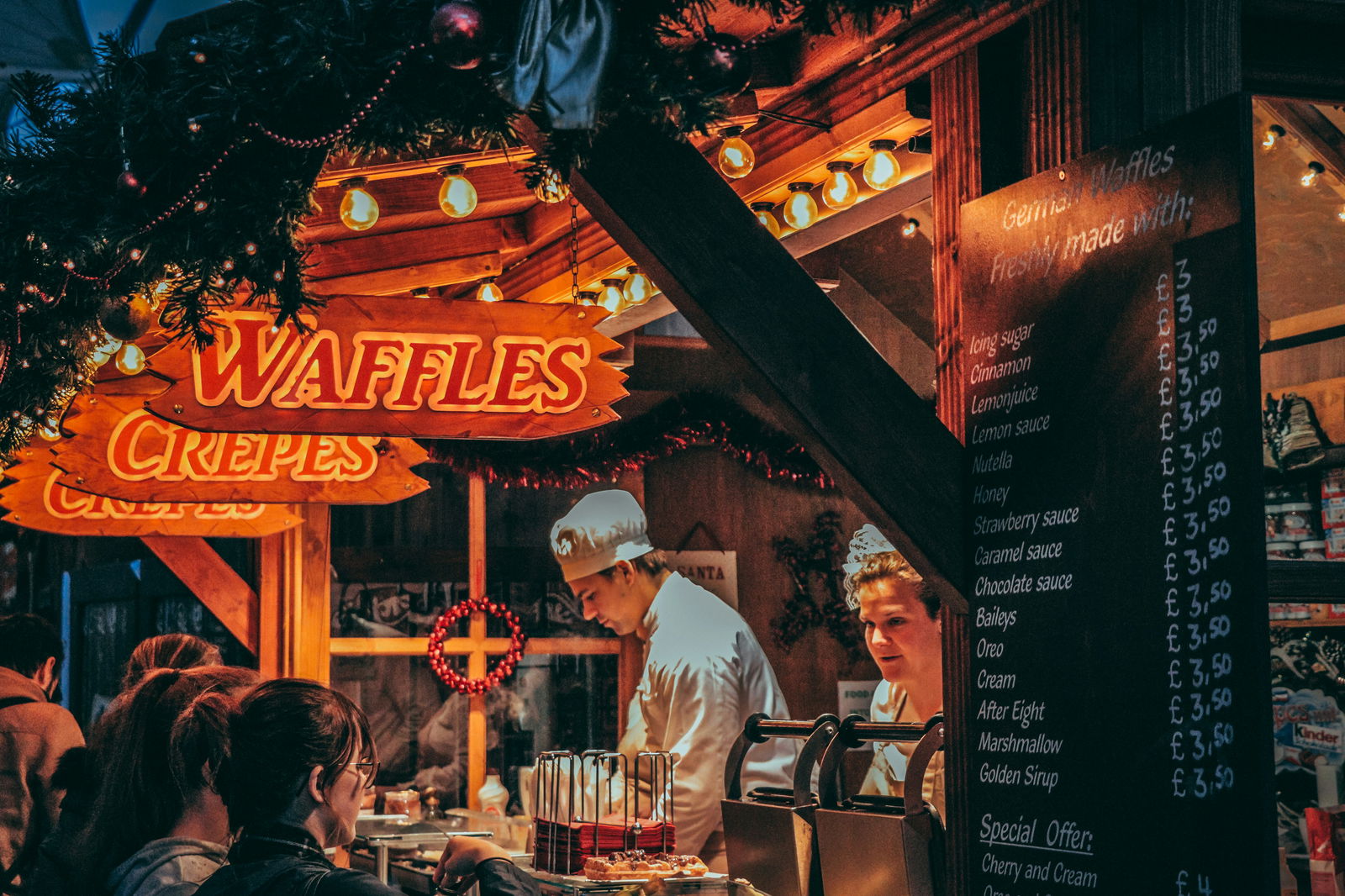 Zwei Waffel-Verkäufer stehen in einem Weihnachtsmarkt-Haus und verkaufen Süßigkeiten zur Weihnachtszeit