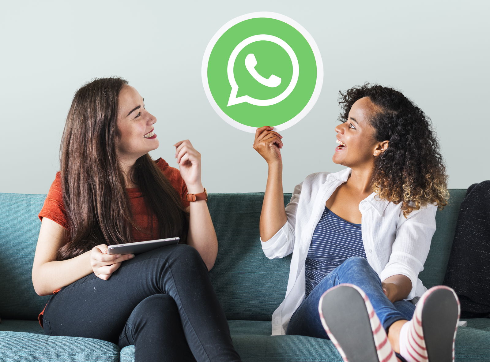 Zwei Frauen sitzen auf einer Couch und schauen ein Whatsapp-Icon an, das zwischen ihnen in der Luft schwebt 