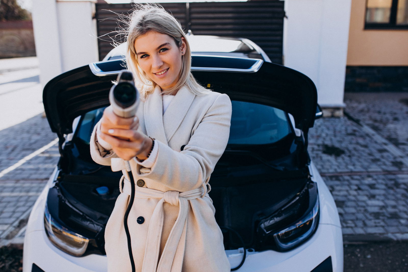 Eine blonde Frau hält das Ladekabel eines Elektrofahrzeuges wie eine Waffe in die Kamera 