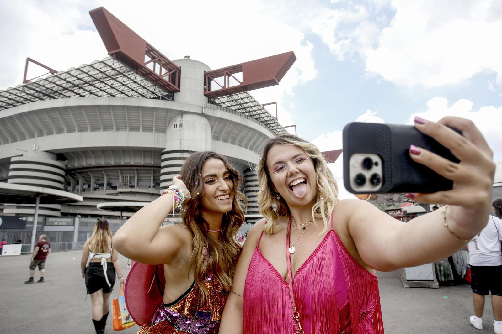 Zwei weibliche Taylor Swift Fans stehen vor einem Stadion in dem Swift ihre Eras-Tour spielt und schießen ein Selfie 