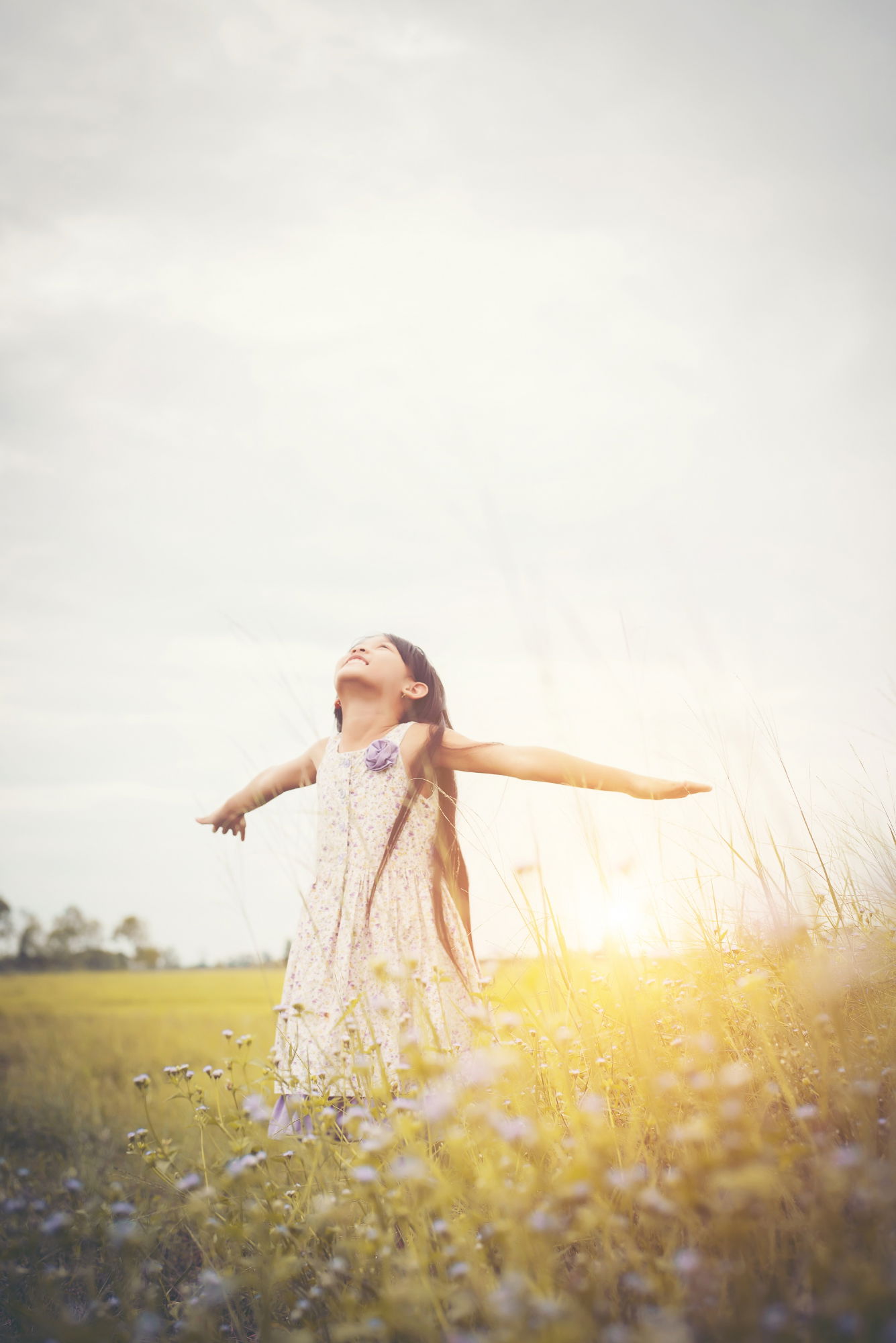 Ein glückliches Kind steht in einem Blumenfeld und hebt die Arme in die Luft 