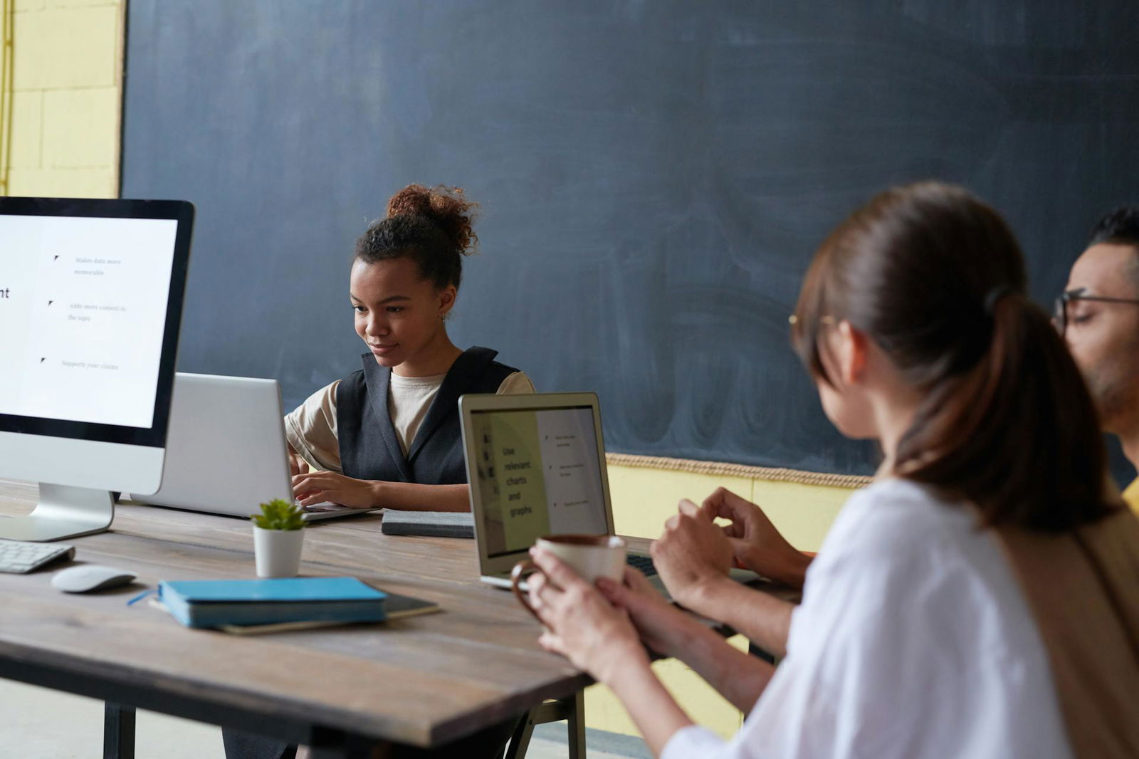 Ein paar Schüler oder Lehrer sitzen in einem Klassenzimmer vor einer Tafel an ihren Computern und arbeiten im Team 