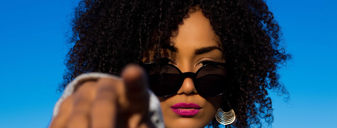 Frau mit Sonnenbrille zeigt in Kamera 