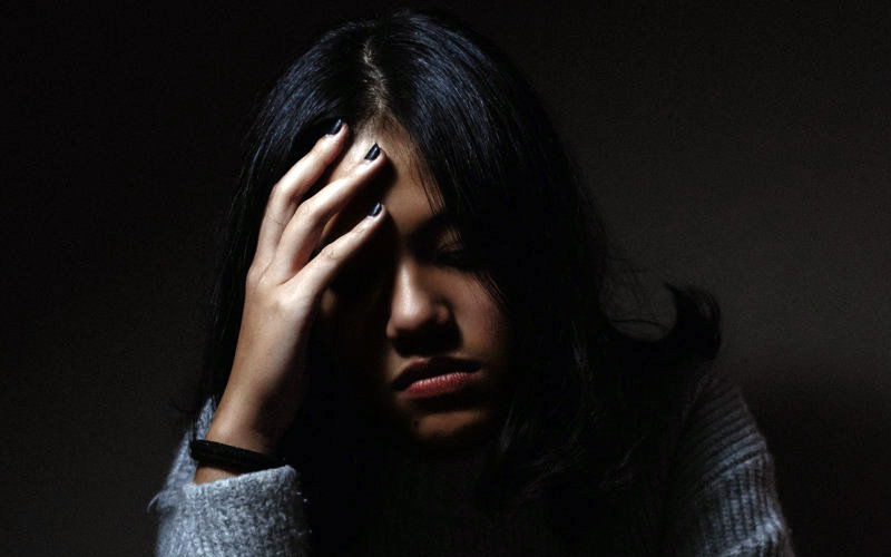 Müdes Mädchen fasst sich an den Kopf und hat Augen geschlossen