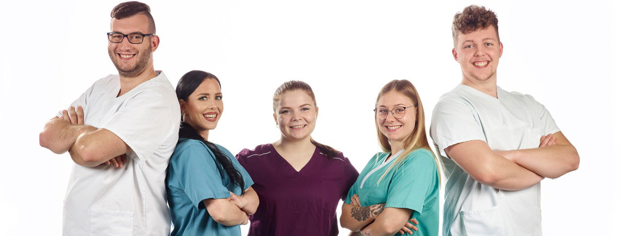 Fünf Ärzte schränken Arme ein und lächeln in Kamera 