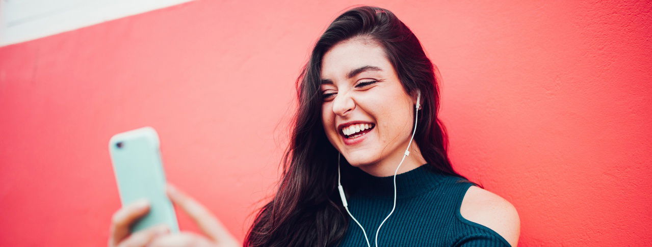 Mädchen mit Kabelkopfhörern im Ohr lacht in Handy hinein 