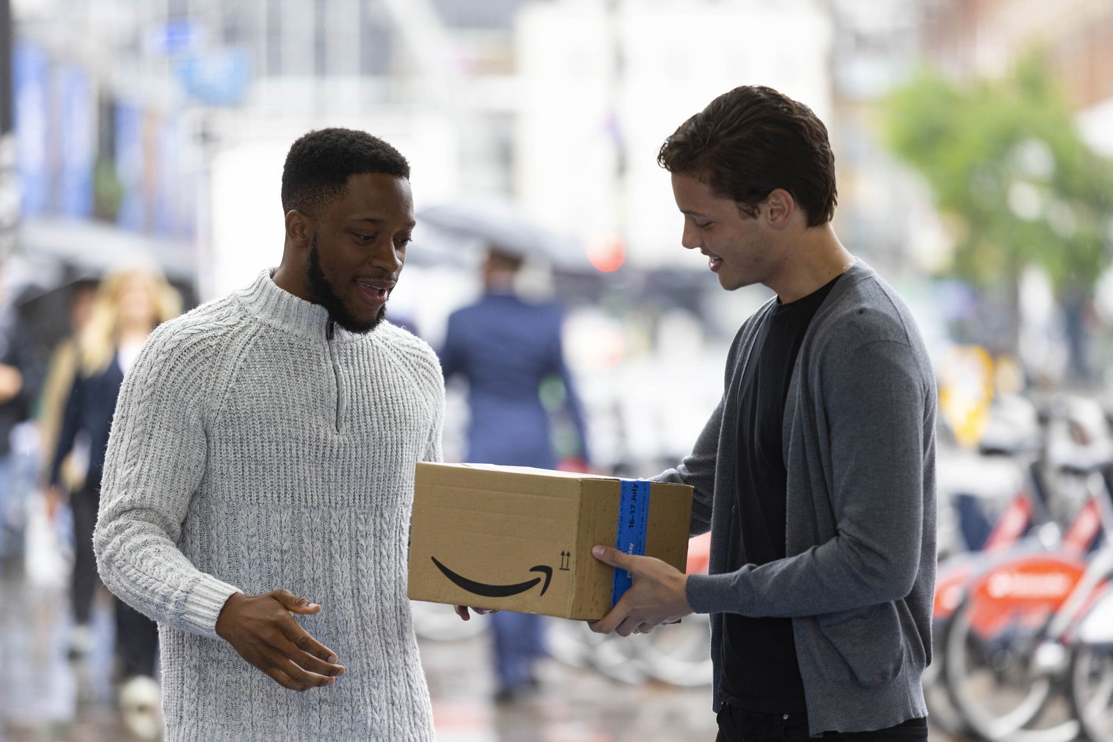 Ein Paketboote übergibt einem dunkelhäutigen Mann ein Amazon-Paket 