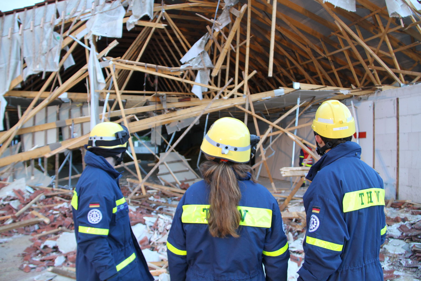 Mitarbeiter und Mitarbeiterinnen des Technischen Hilfswerks stehen vor den Trümmern eines Hauses 