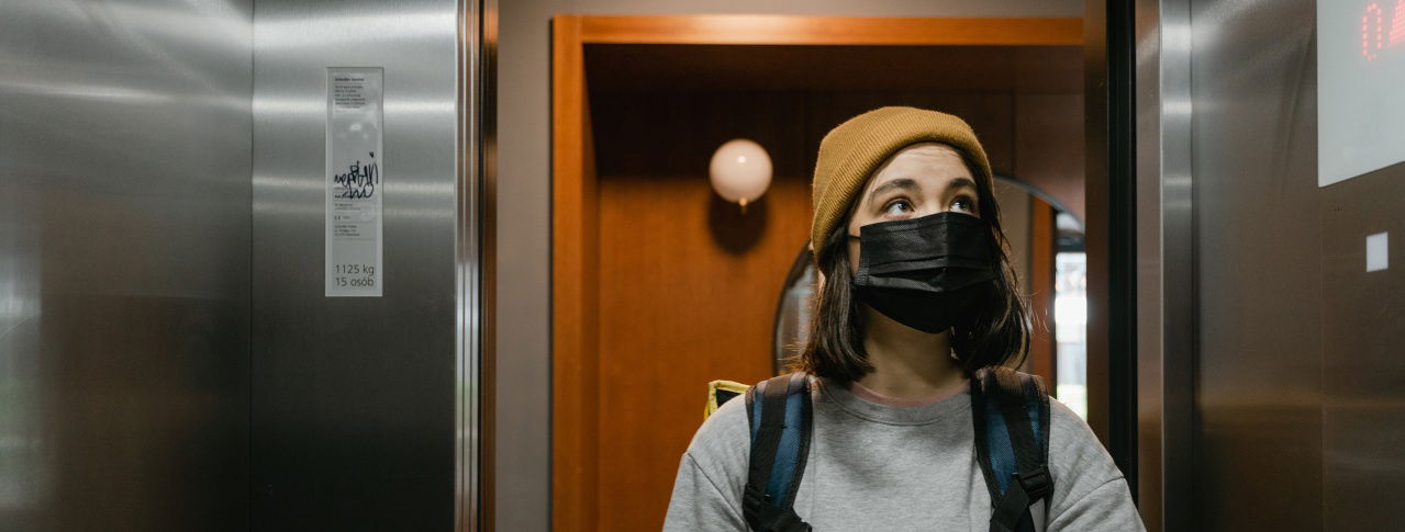 Frau mit Maske vor Aufzug 