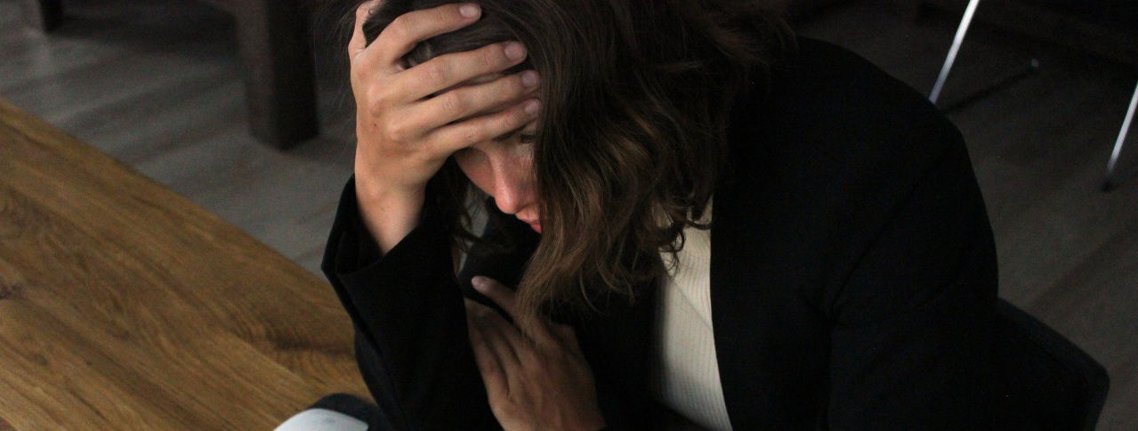 Verzweifelte Frau hält sich mit der Hand den Kopf und sitzt am Tisch