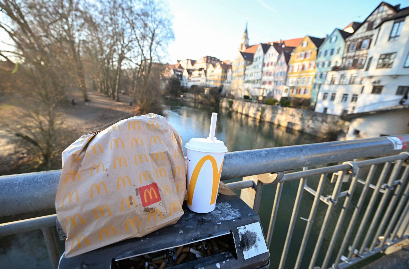 Eine McDonald's To-Go-Tüte und ein To-Go-Becher werden auf der Neckarbrücke in Tübingen vor der Kulisse der Altstadt gehalten (gestellte Szene).