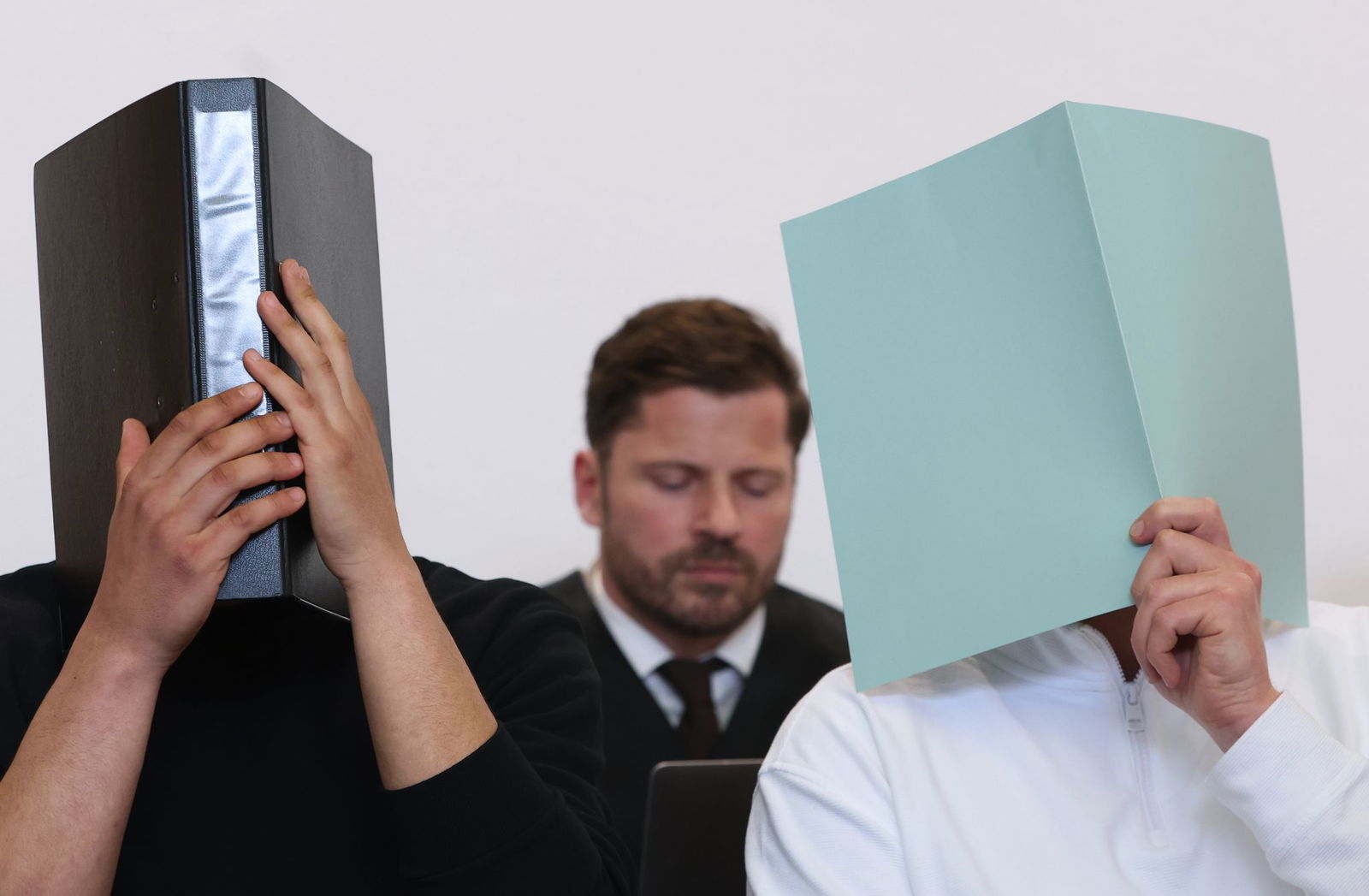 Der Hauptangeklagte (r) sitzt in einem Gerichtssaal neben weiteren Angeklagten vor Rechtsanwalt Harald Stehr (M) auf der Anklagebank. Der Mann wurde wegen eines Böllerwurfs mit zwölf Verletzten zu einer Gefängnisstrafe verurteilt, das Urteil ist nun rech…