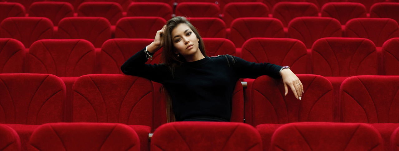 Mädchen sitzend im Kinosaal, stützt Kopf auf Arm ab