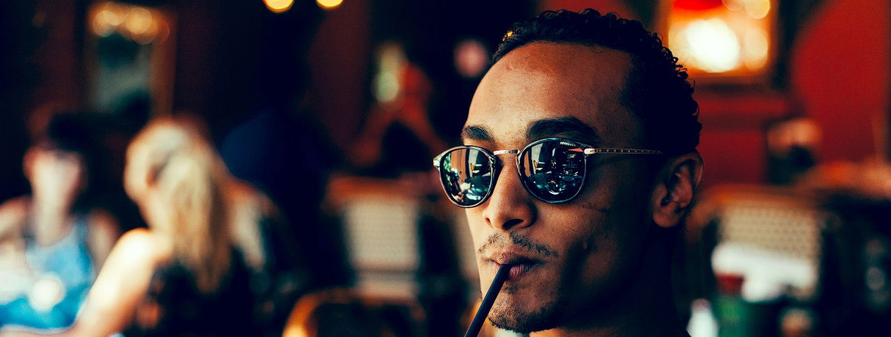 Mann mit Sonnebrille hat Strohhalm im Mund 