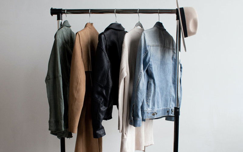 Kleiderstange mit 5 Jacken und einem weißen Hut an der rechten Seite