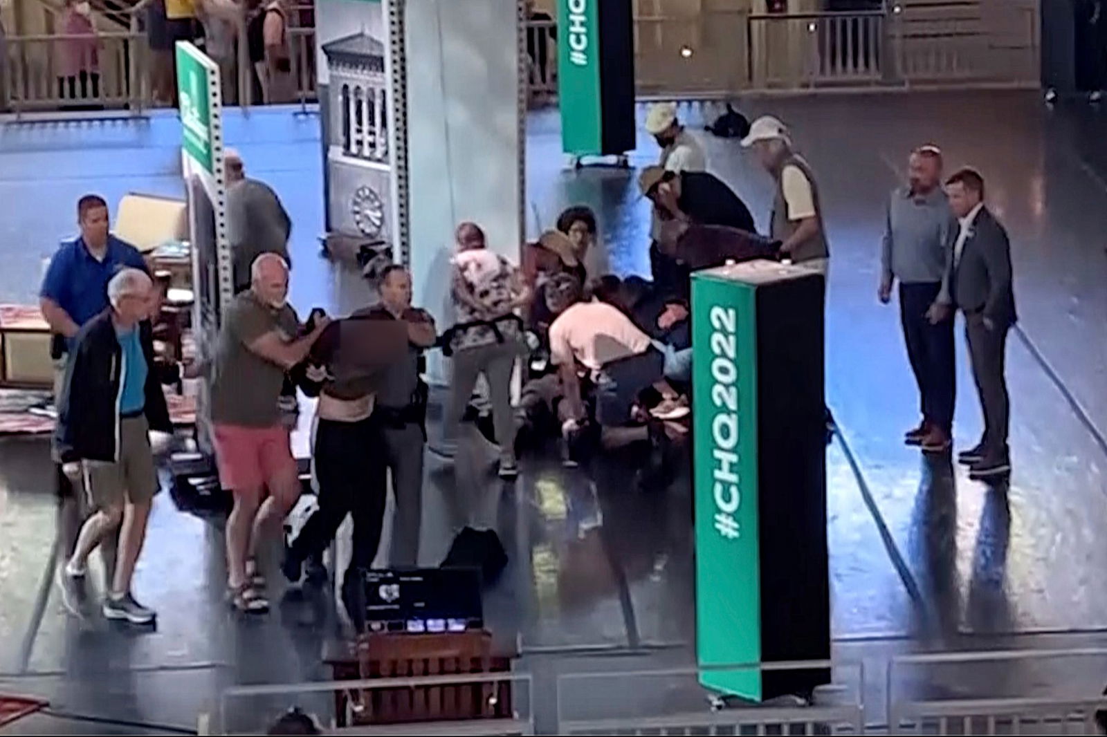 Menschen kümmern sich um den verletzten Rushdie, während ein Mann von der Bühne eskortiert wird. (Aufnahme kurz nach dem Angriff)