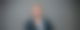 Nachdenklicher Mann vor grauen Wand, Zeigefinger vorm Mund und schaut in Kamera