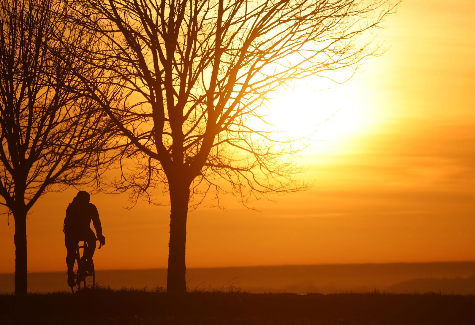 Ein Radfahrer ist am Morgen kurz nach Sonnenaufgang unterwegs, während sich der Himmel durch den Saharastaub in Orangetönen verfärbt hat.