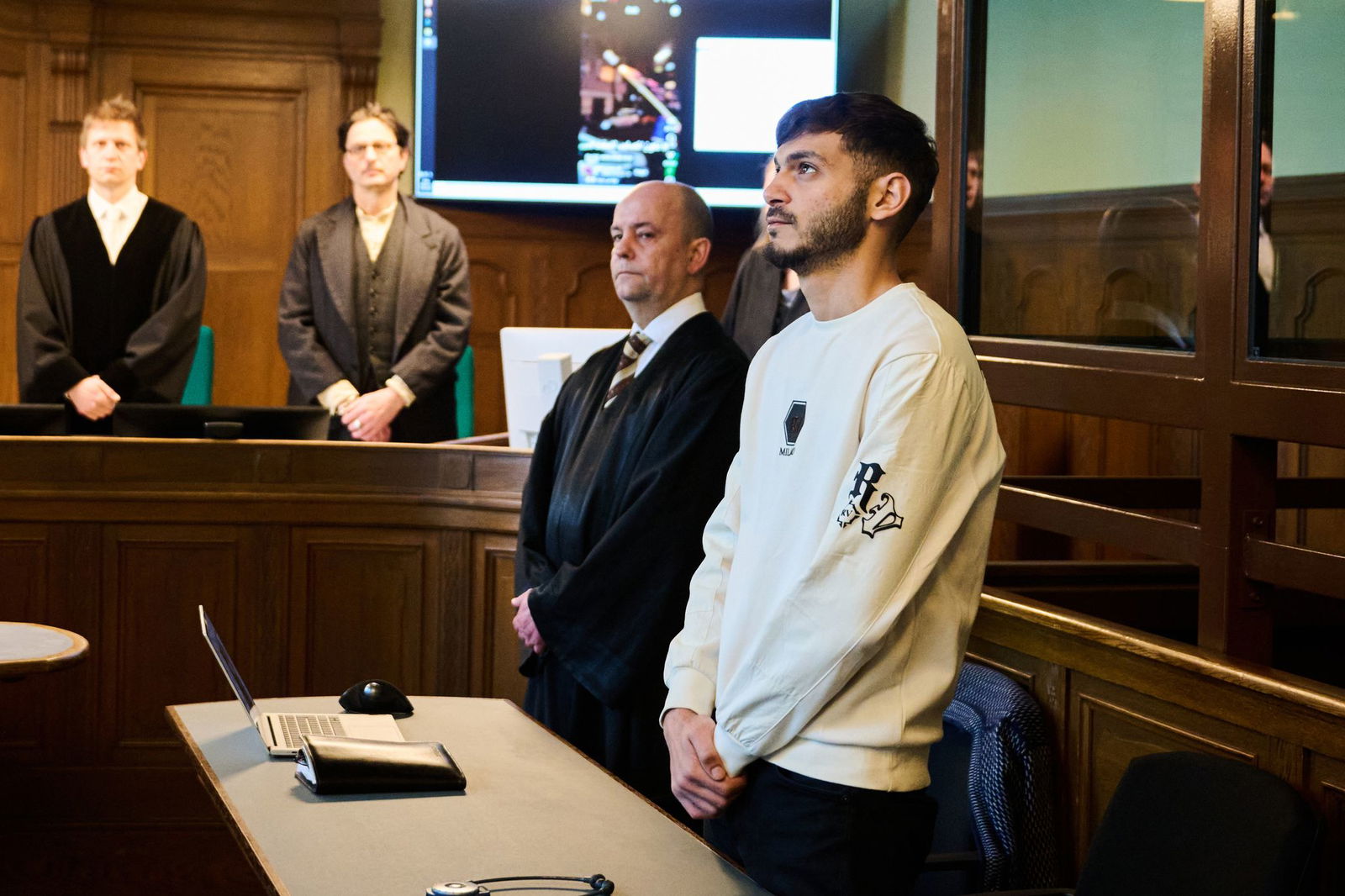 Der Influencer (r), der eine Silvesterrakete in eine Wohnung geschossen hat, steht mit gefalteten Händen im Gerichtssaal neben seinem Rechtsanwalt.
