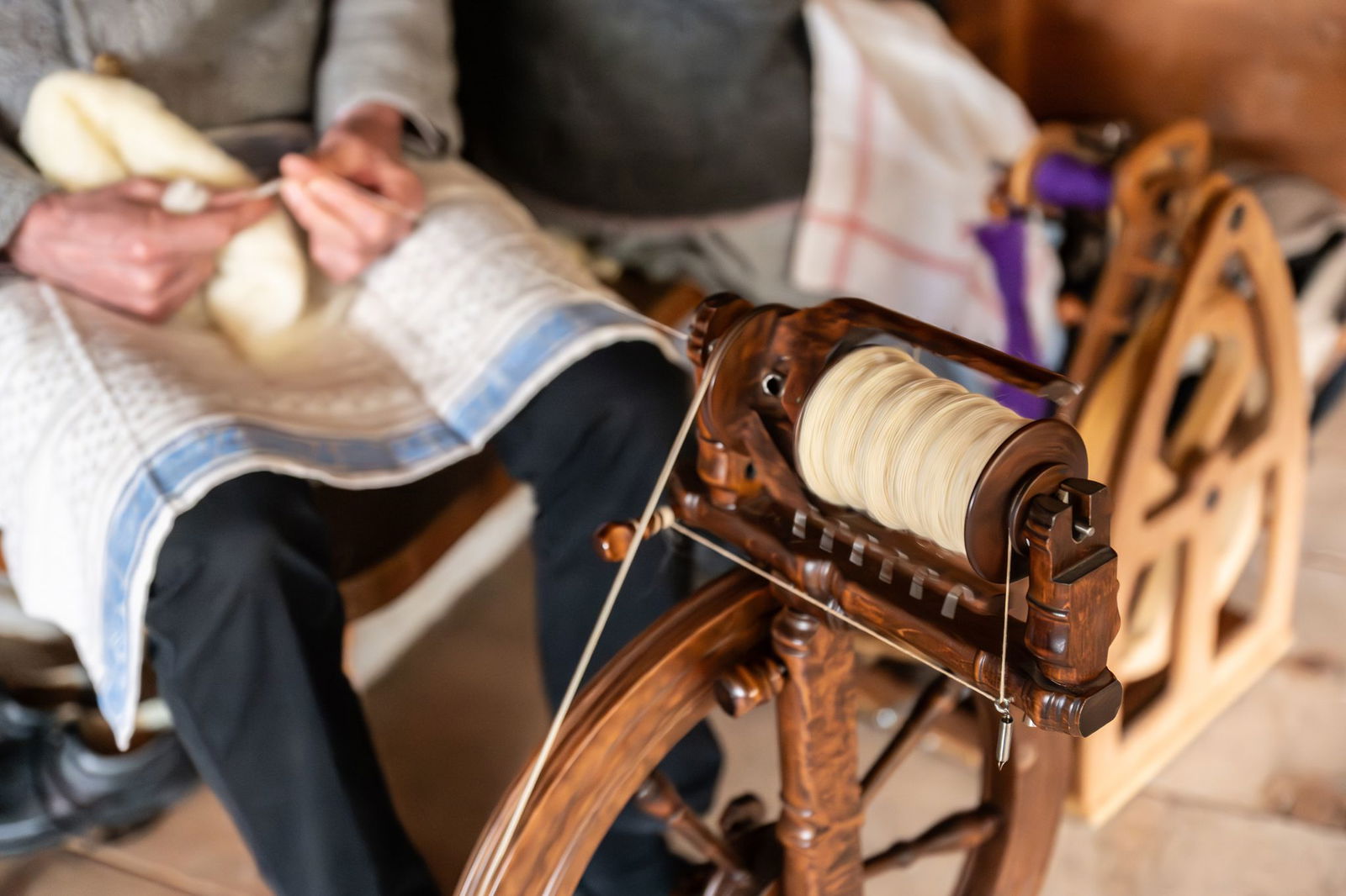 Ein Mann spinnt in einem Gebäude auf dem Gelände des Vogtsbauernhofs im Schwarzwälder Freilichtmuseum Garn mit einer Spindel.