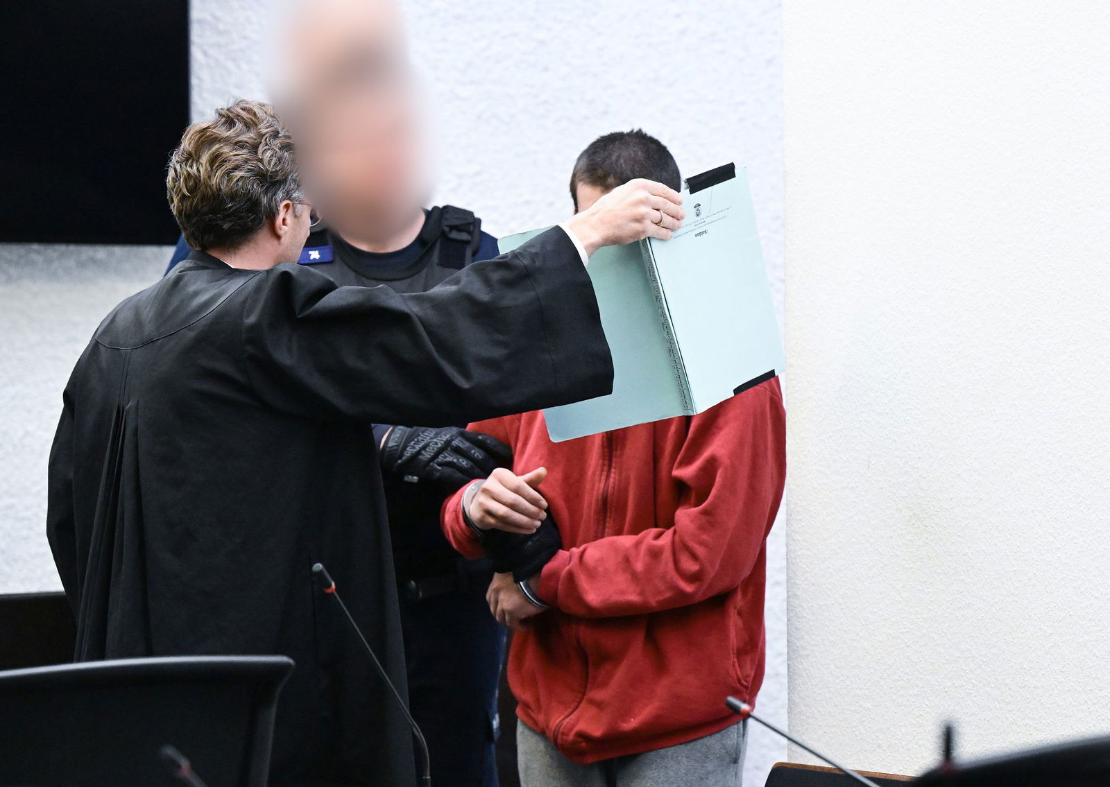 In Hand- und Fußfesseln gesichert, von seinem Verteidiger abgeschirmt, wird der angeklagte Flüchtling nach dem tödlichen Messerangriff auf einen Jogger in Hochdorf zur Anklagebank geführt. 