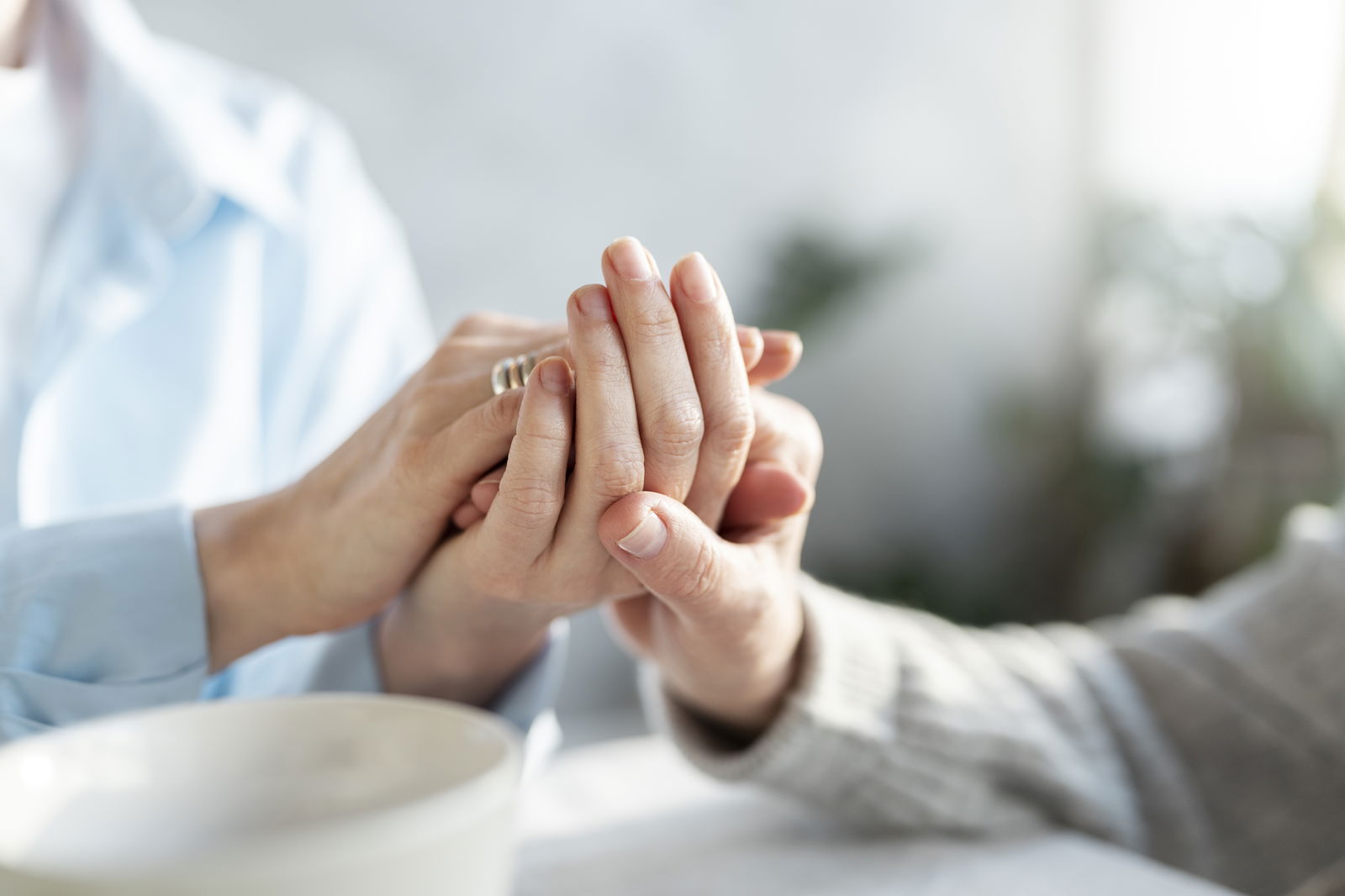 Pflegende Person hält die Hände eines älteren Mannes als Zeichen des Mitgefühls