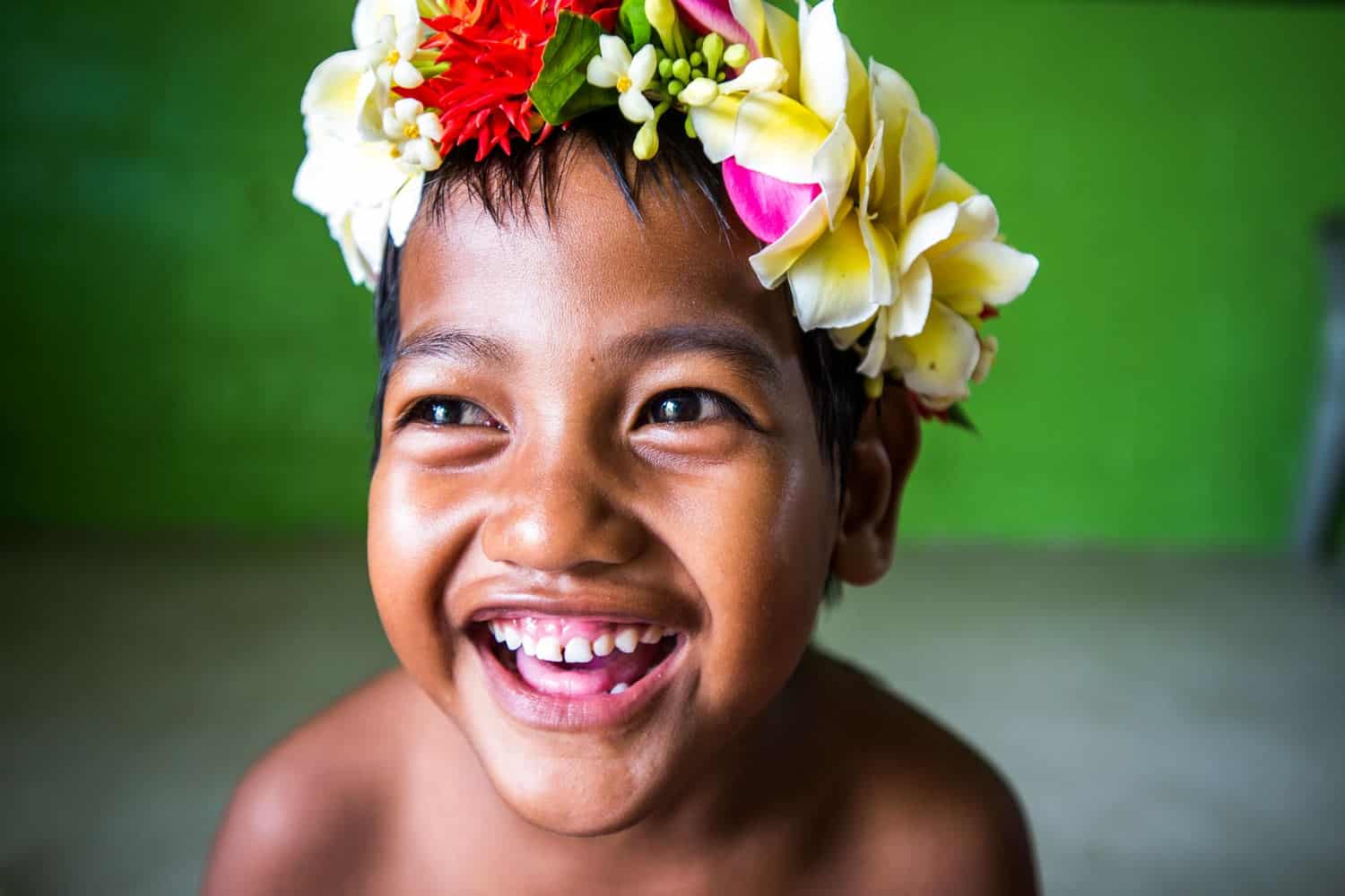 Ein kleiner Junge aus Tuvalu lacht fröhlich in die Kamera. Er trägt eine Blumenkrone 