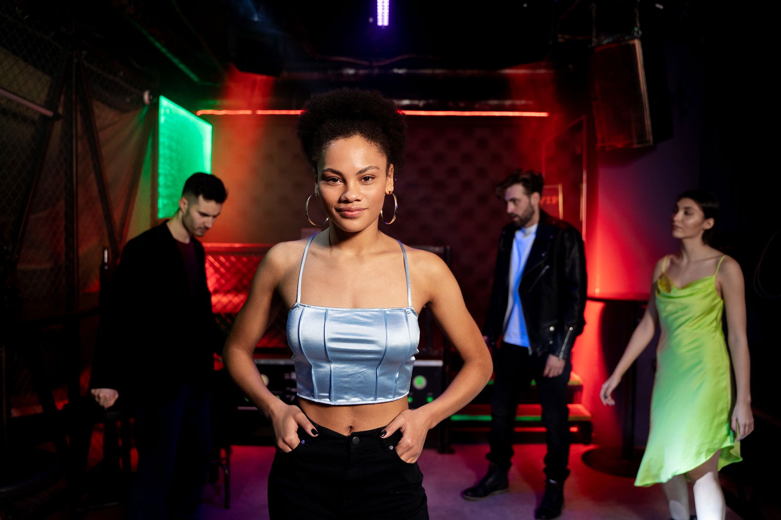 Awareness-Konzept in Wiener Clubs ab 2026 Pflicht: Eine junge Frau steht selbstbewusst in einem Club mit bunter Lichtstimmung und blickt direkt in die Kamera. Im Hintergrund sind drei weitere Personen zu sehen – zwei Männer und eine Frau –, die sich im Ra