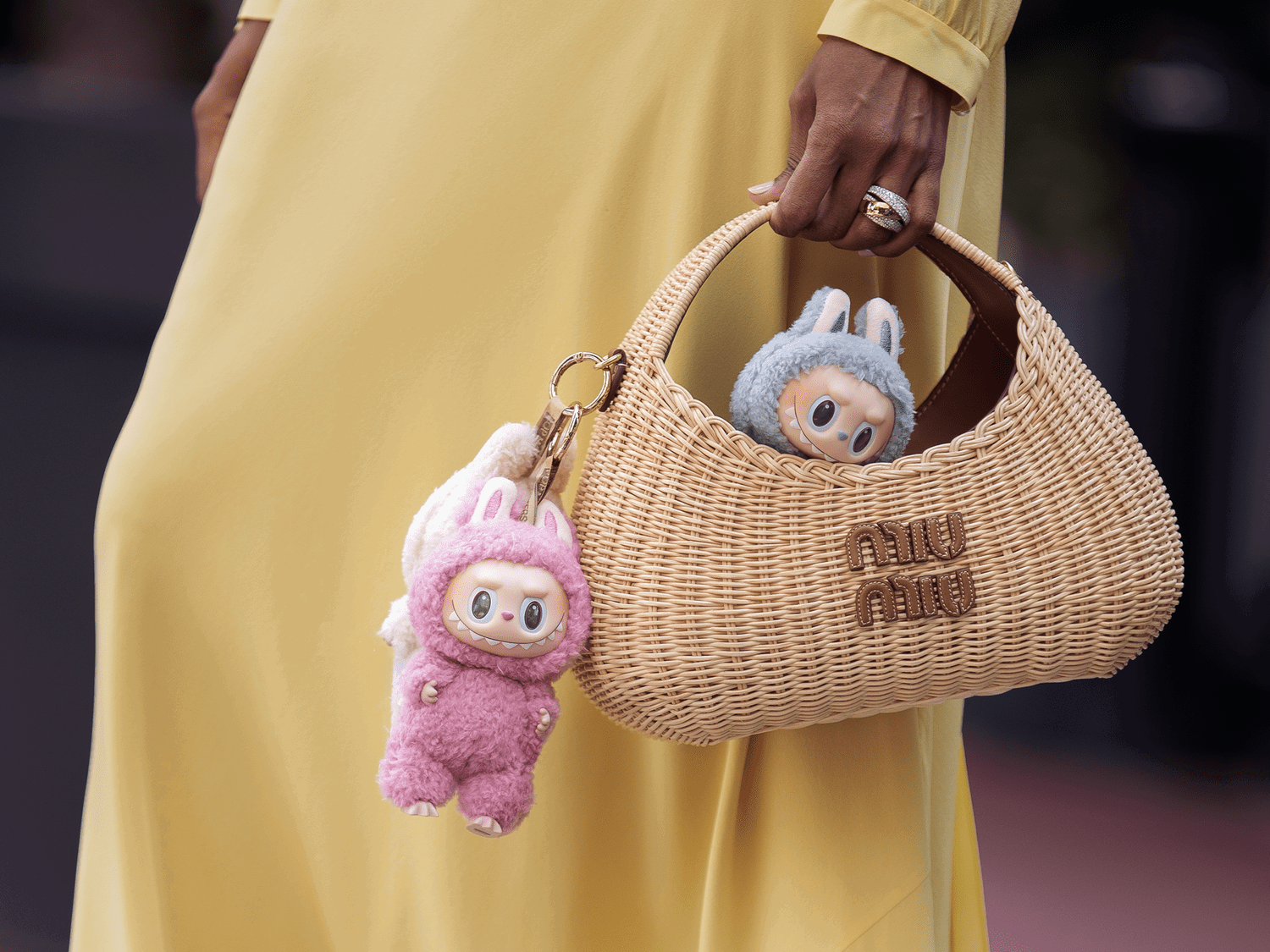 Eine rosane und eine weiße Labubu-Doll hängen an und sitzen in einer Miu-Miu-Korb-Tasche einer Mode-Influencerin 