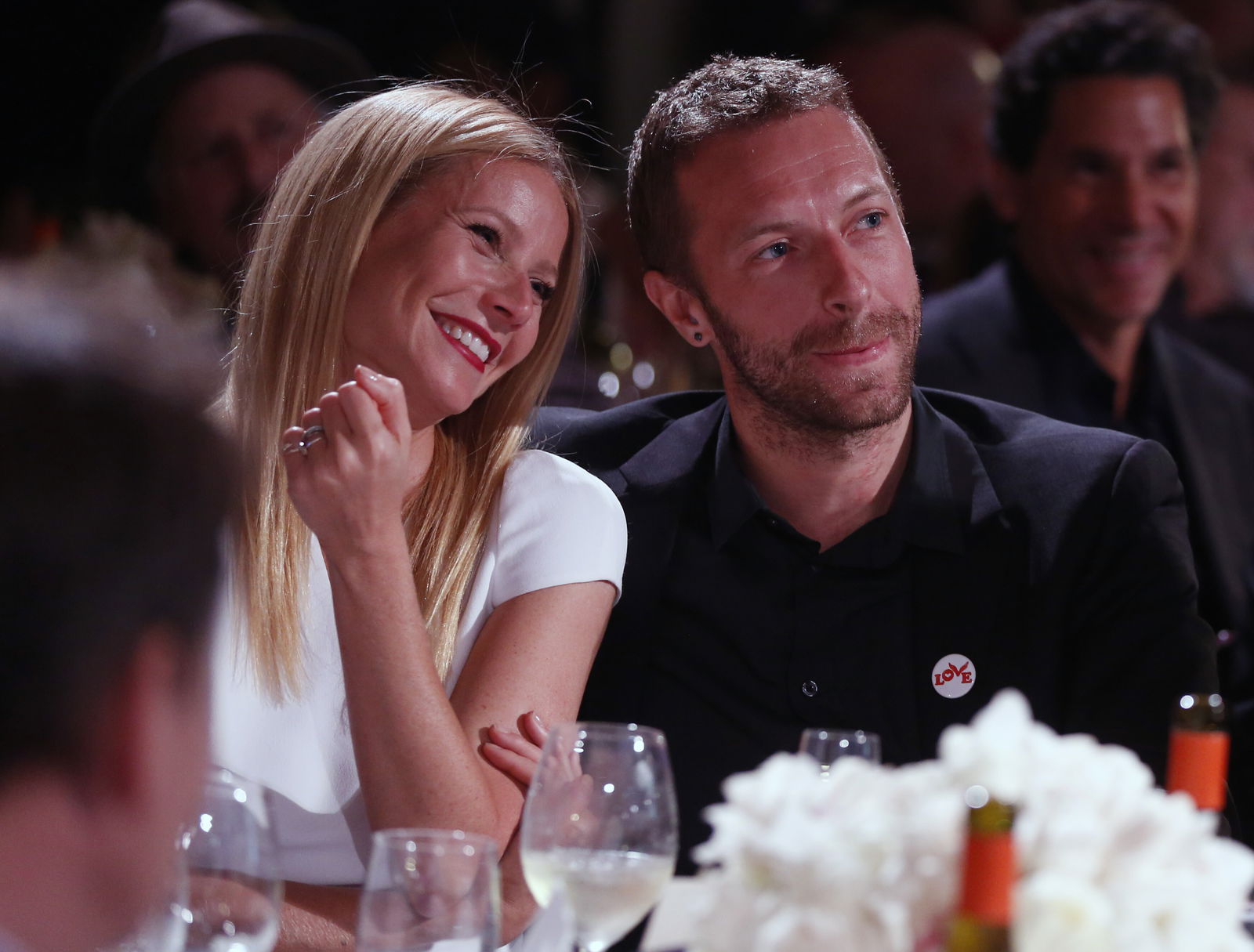 Gwyneth Paltrow und Chris Martin sitzen 2014 bei einer Abendveranstaltung nebeneinander, lächeln und wirken vertraut. Beide tragen elegante Kleidung und sitzen an einem festlich gedeckten Tisch.