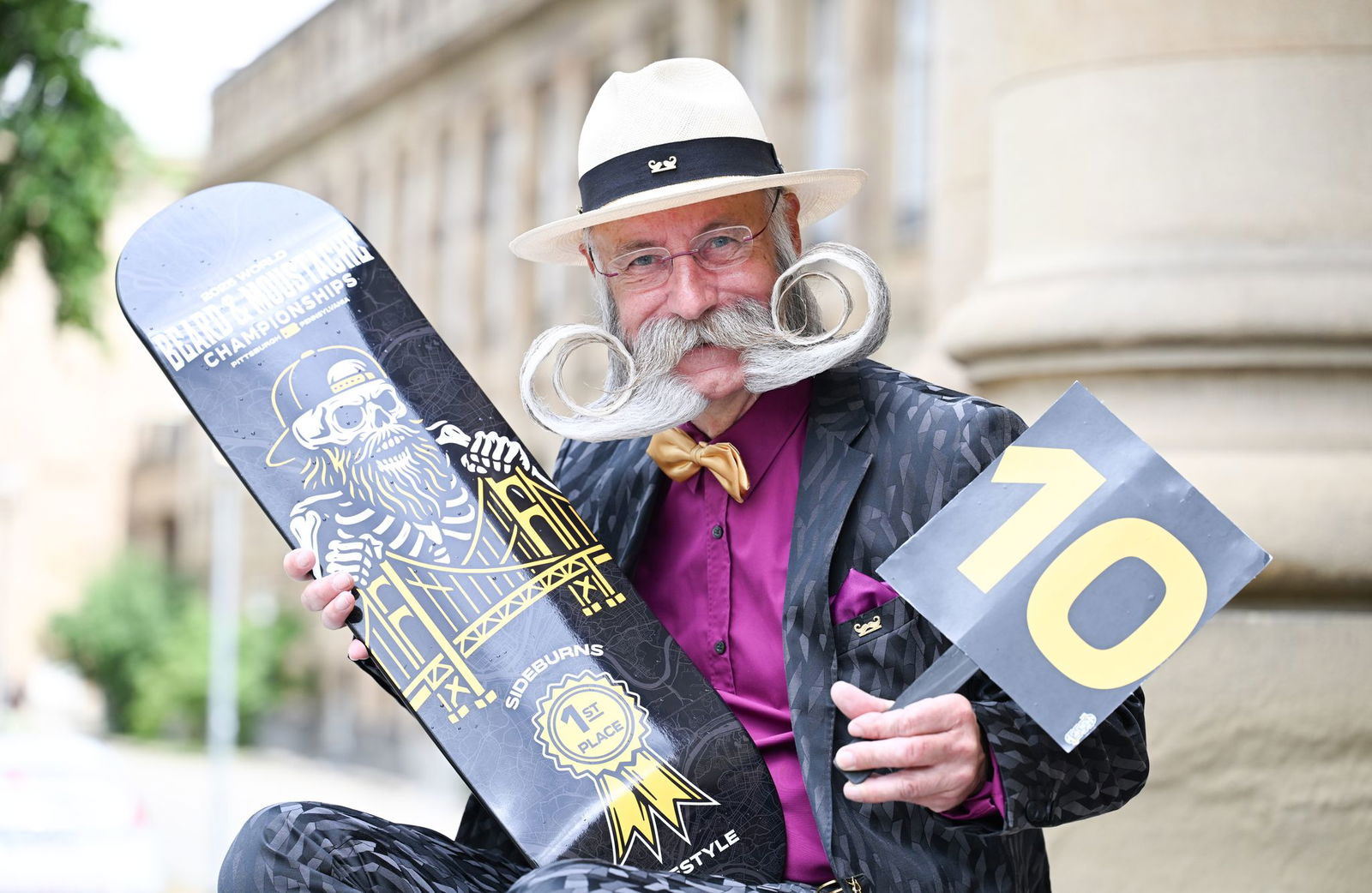 Er präsentiert seine Siegertrophäe und eine Wertungstafel mit der Maximalpunktzahl 10. 