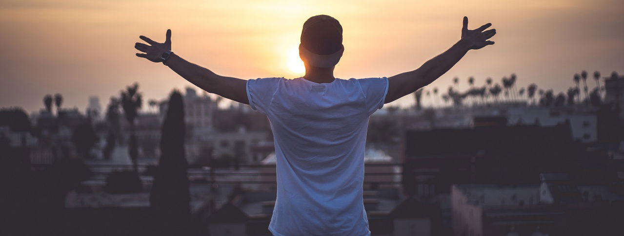 mann mit cap breitet hände vor sonnenuntergang aus